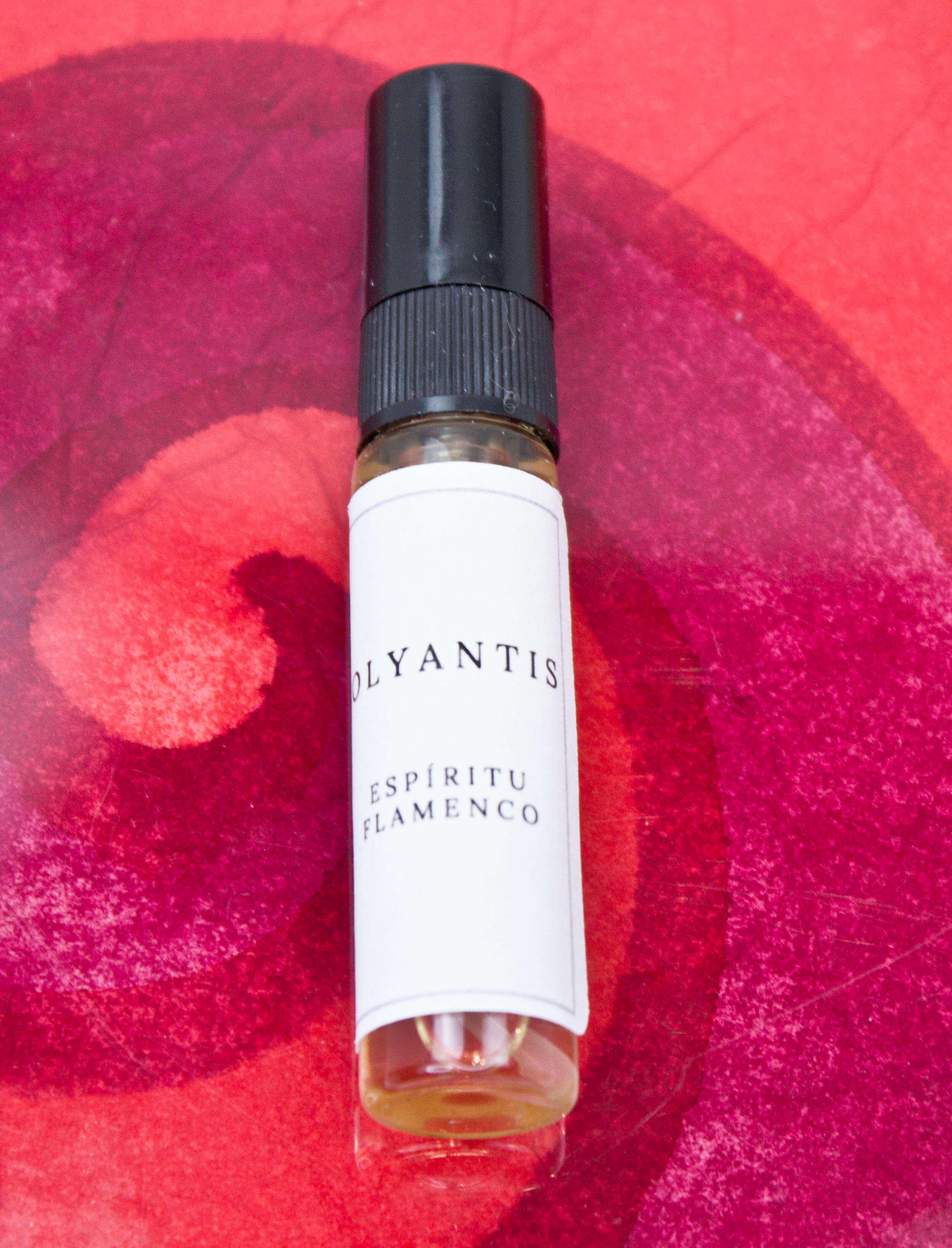 Olyantis's Espíritu Flamenco 5 ml perfume glass bottle on a red-burgundy colorful background.