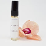 Olyantis's Espíritu Flamenco 5 ml perfume glass bottle beside a golden-burgundy flower.