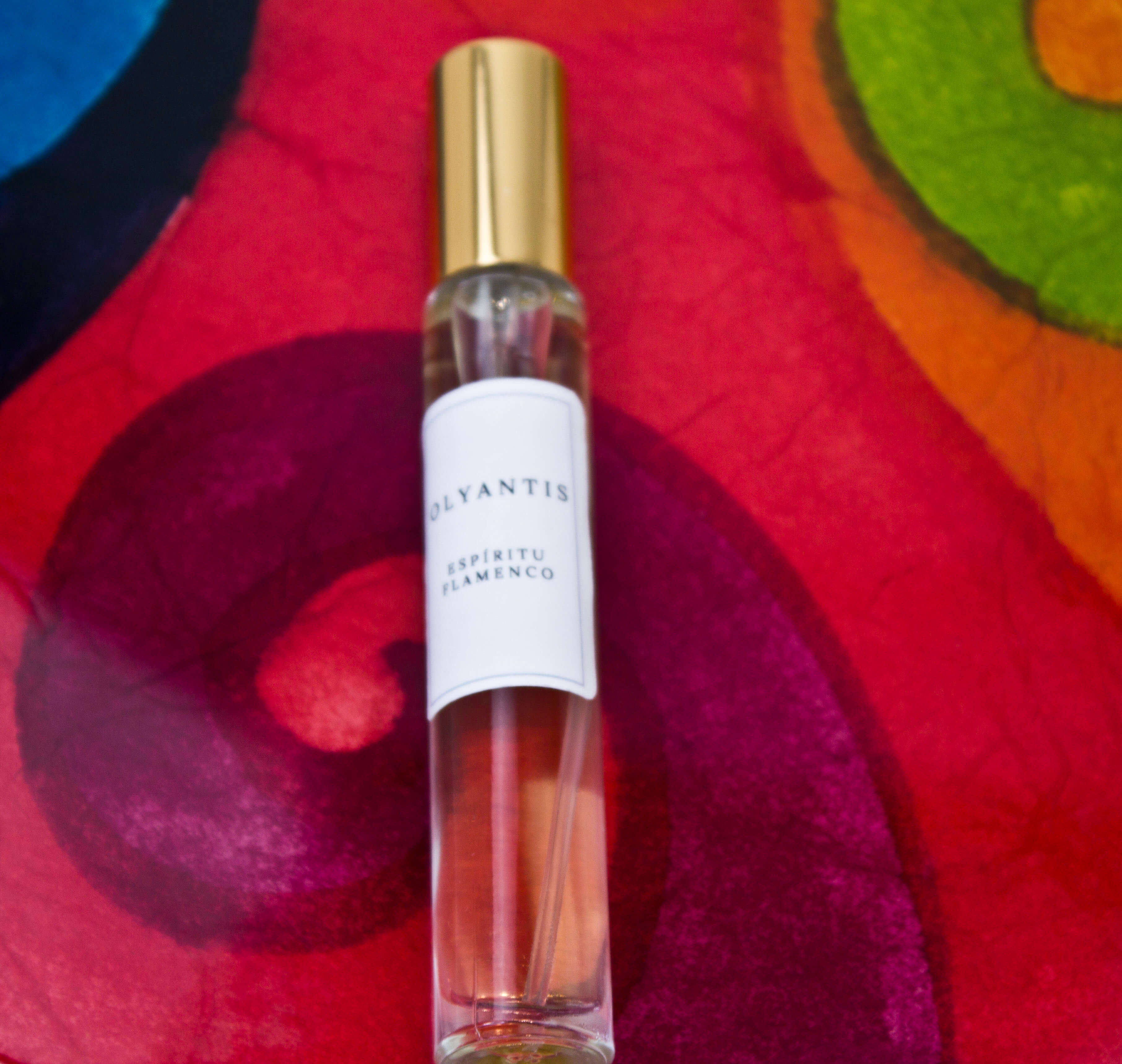 Olyantis's Espíritu Flamenco 10 ml perfume glass bottle with gold cap on a red-burgundy colorful background.