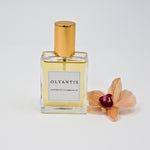 Olyantis's Espíritu Flamenco 60 ml perfume glass bottle with gold cap beside a golden-burgundy flower.