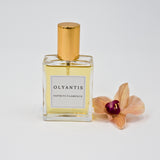 Olyantis's Espíritu Flamenco 60 ml perfume glass bottle with gold cap beside a golden-burgundy flower.