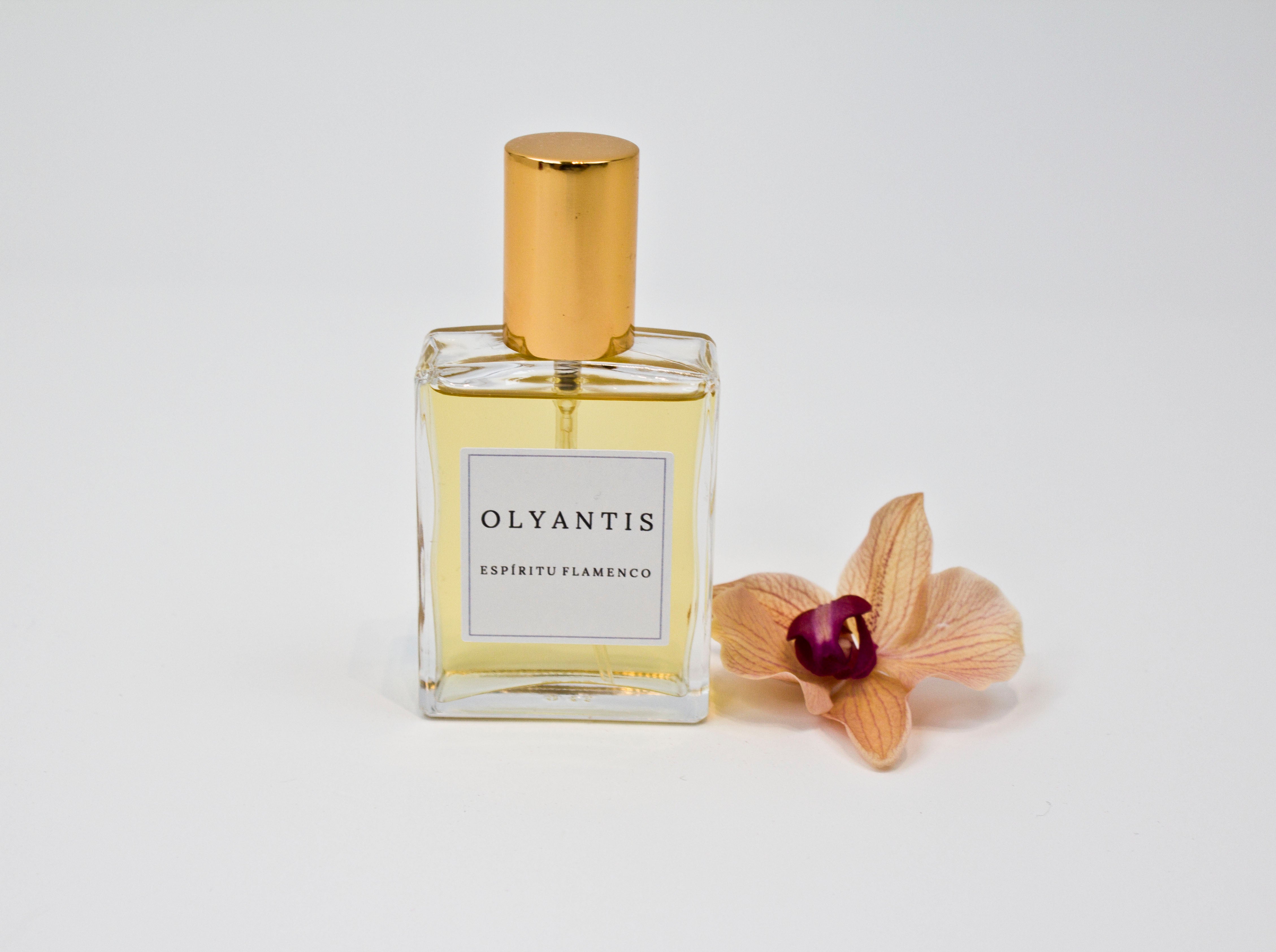 Olyantis's Espíritu Flamenco 60 ml perfume glass bottle with gold cap beside a golden-burgundy flower.