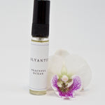 Olyantis's Peaceful Ocean 5 ml perfume glass bottle beside a white-purple flower.
