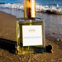 Olyantis 60 ml Peaceful Ocean eau de parfum bottle, on a beach with waves in the background. 