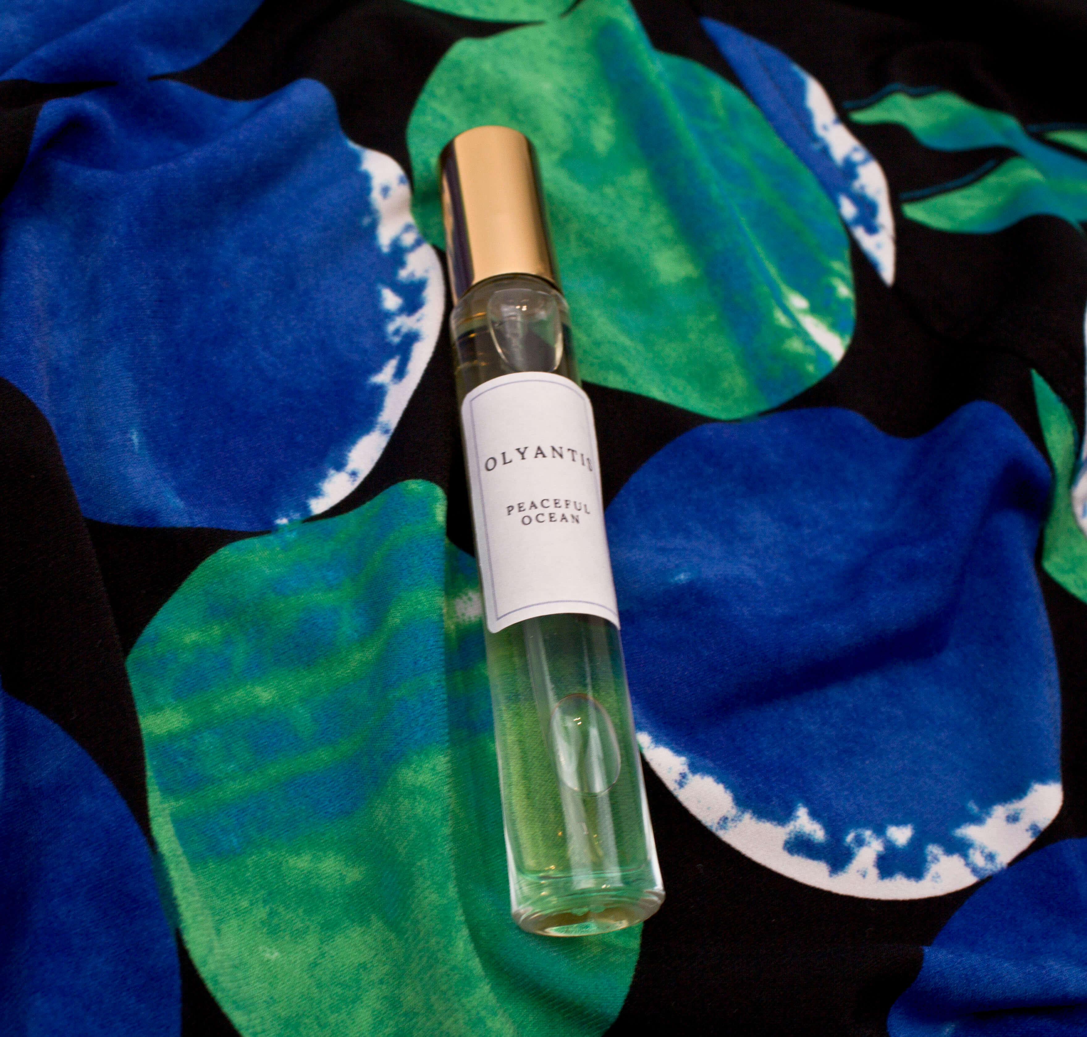 Olyantis's Peaceful Ocean 10 ml perfume glass bottle with gold cap on the intense blue and green background. 