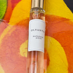 Olyantis's  Rapsodie D'Été 10 ml perfume glass bottle with gold cap on an orange, colorful background.