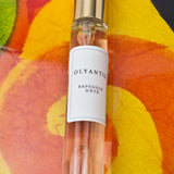 Olyantis's  Rapsodie D'Été 10 ml perfume glass bottle with gold cap on an orange, colorful background.