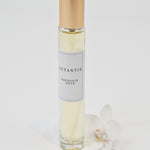 Olyantis's  Rapsodie D'Été 10 ml perfume glass bottle with gold cap beside a white flower.