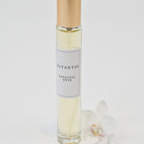 Olyantis's  Rapsodie D'Été 10 ml perfume glass bottle with gold cap beside a white flower.