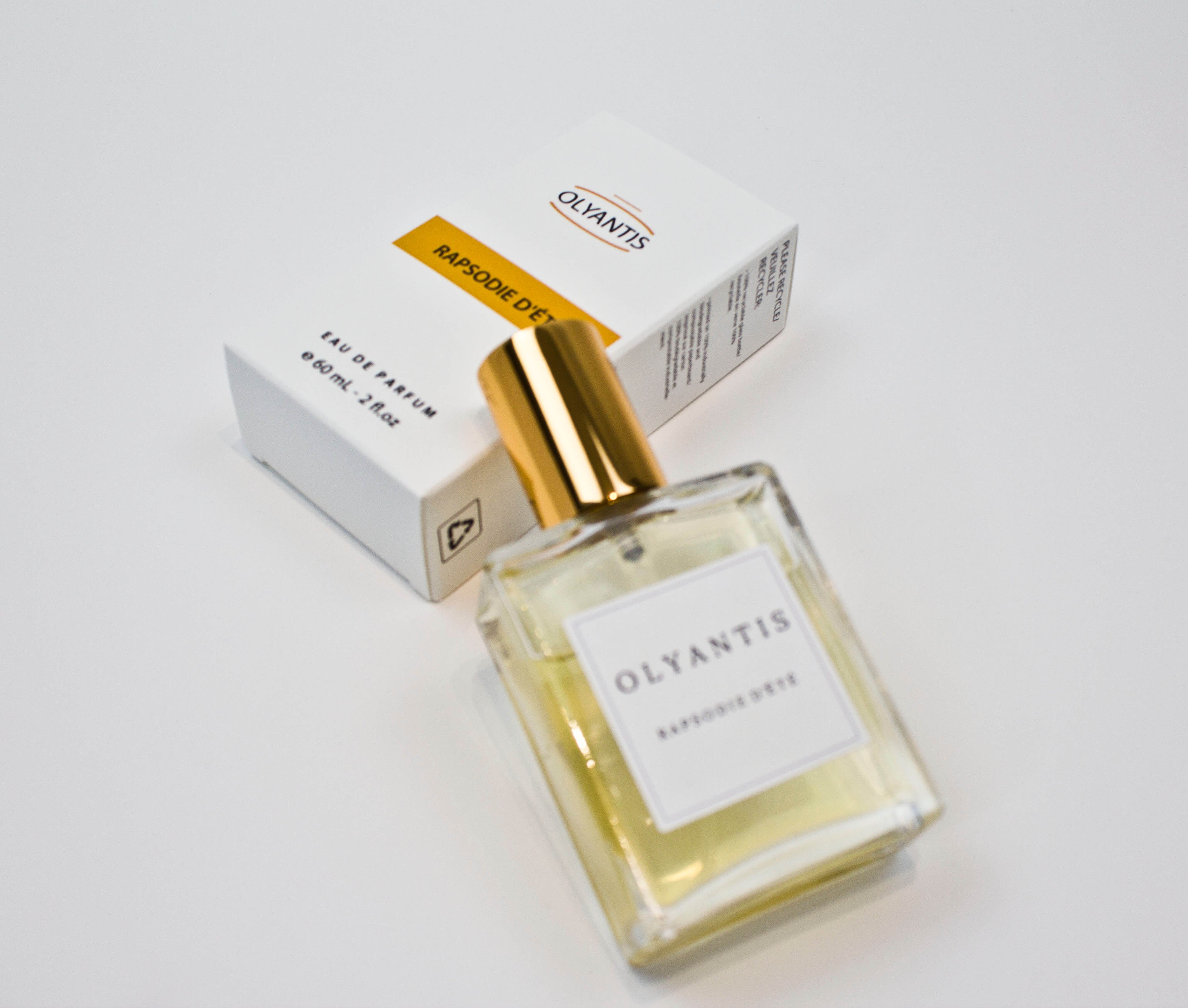 Olyantis's  Rapsodie D'Été 60 ml perfume glass bottle with gold cap beside its paper box.