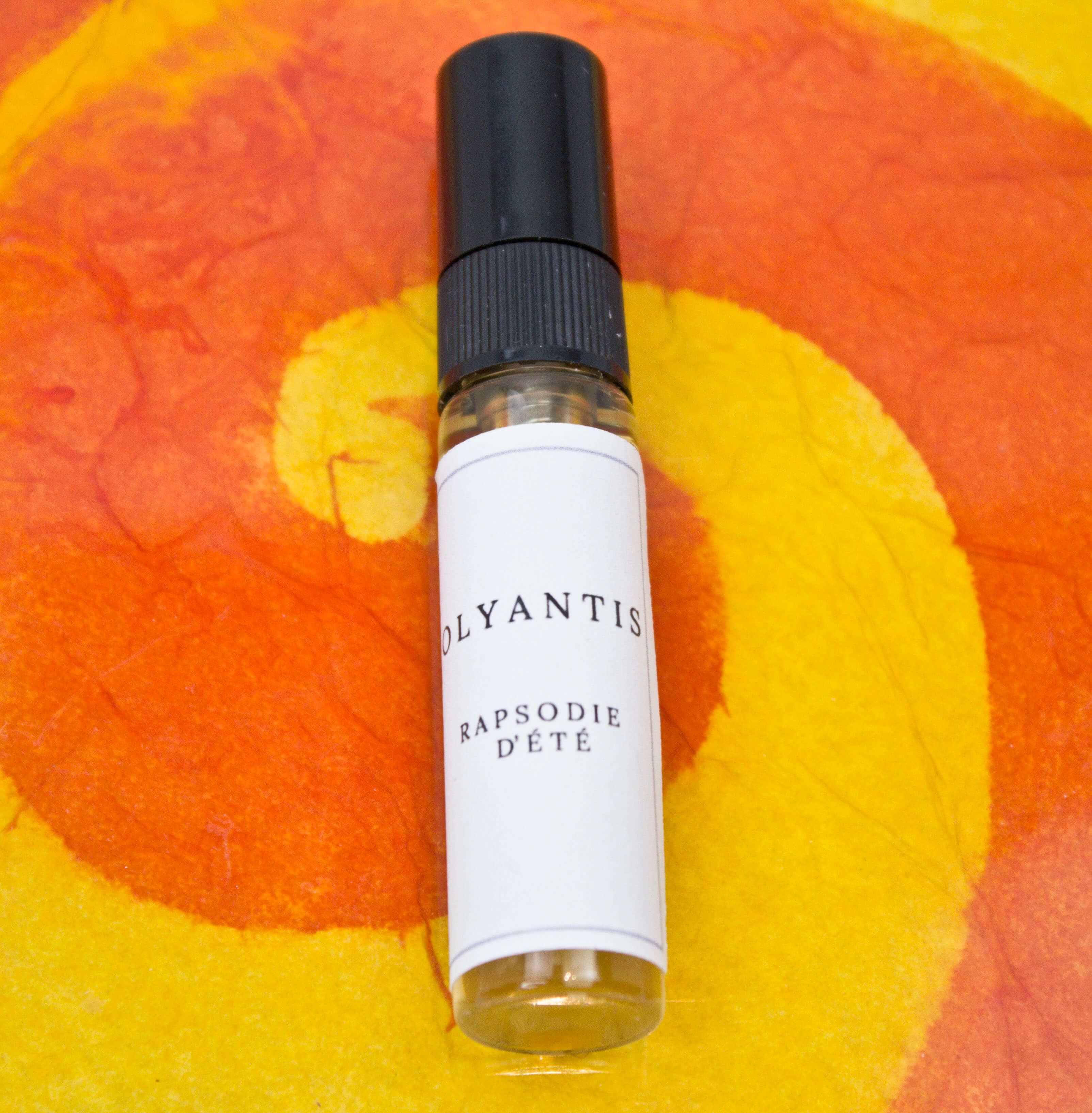 Olyantis's  Rapsodie D'Été 5 ml perfume glass bottle on an orange, colorful background.