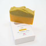 Rapsodie D'Été handmade, plant-based soap in a two-tone, sage and orange color, standing upright on top of its white cardboard packaging box against a clean white background.