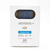 A white rectangular box of Olyantis's Peaceful Ocean plant-based soap, featuring a circular cutout window showing the dark blue soap bar inside. The packaging includes text detailing the scent and ingredients. Made in Canada