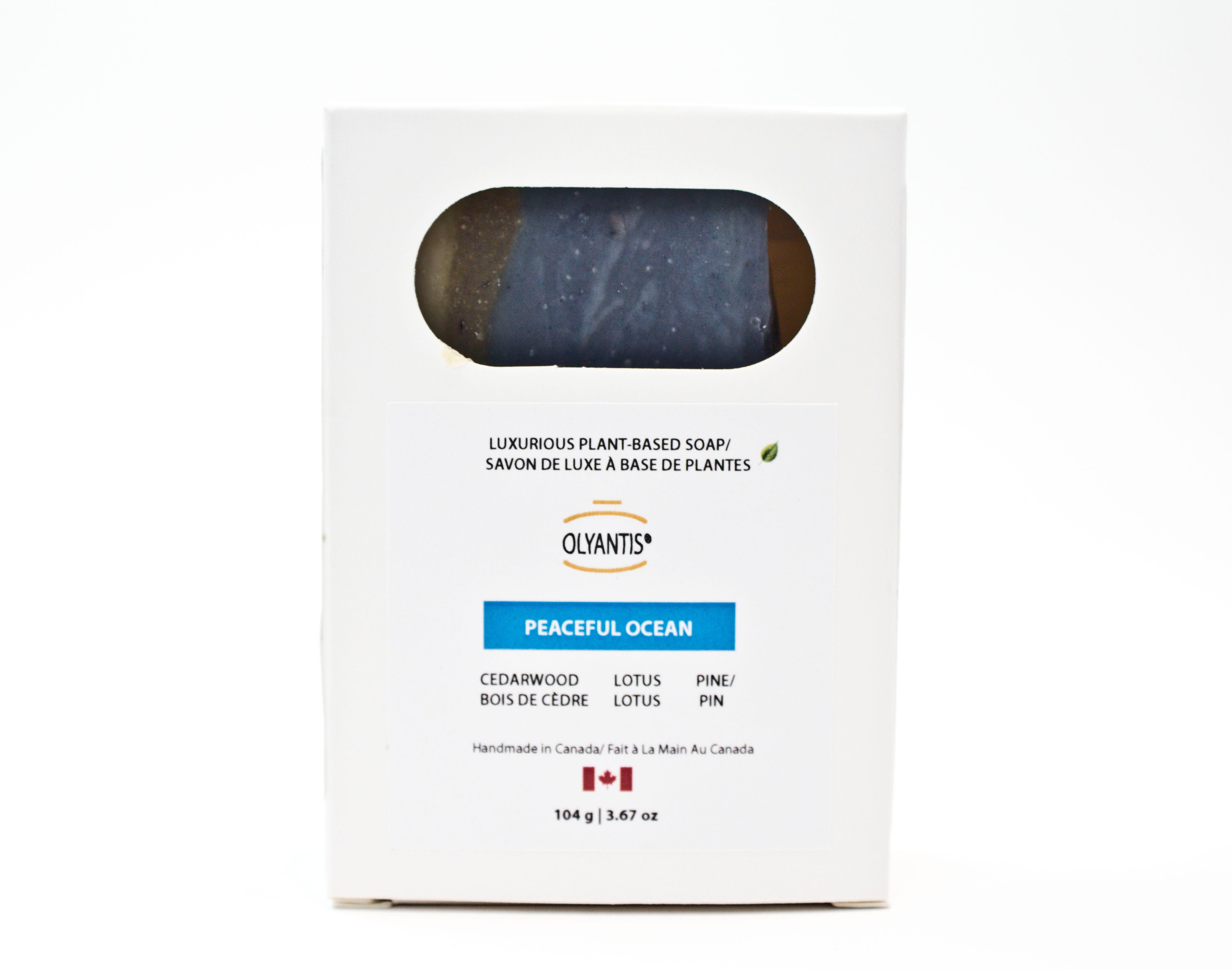 A white rectangular box of Olyantis's Peaceful Ocean plant-based soap, featuring a circular cutout window showing the dark blue soap bar inside. The packaging includes text detailing the scent and ingredients. Made in Canada
