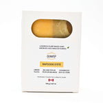 A white rectangular box of Olyantis's Rapsodie D'Eté  soap (cedarwood, linden, balsam poplar scent) with a window showing the  sage-golden-yellow bar of soap inside, set against a plain white background.