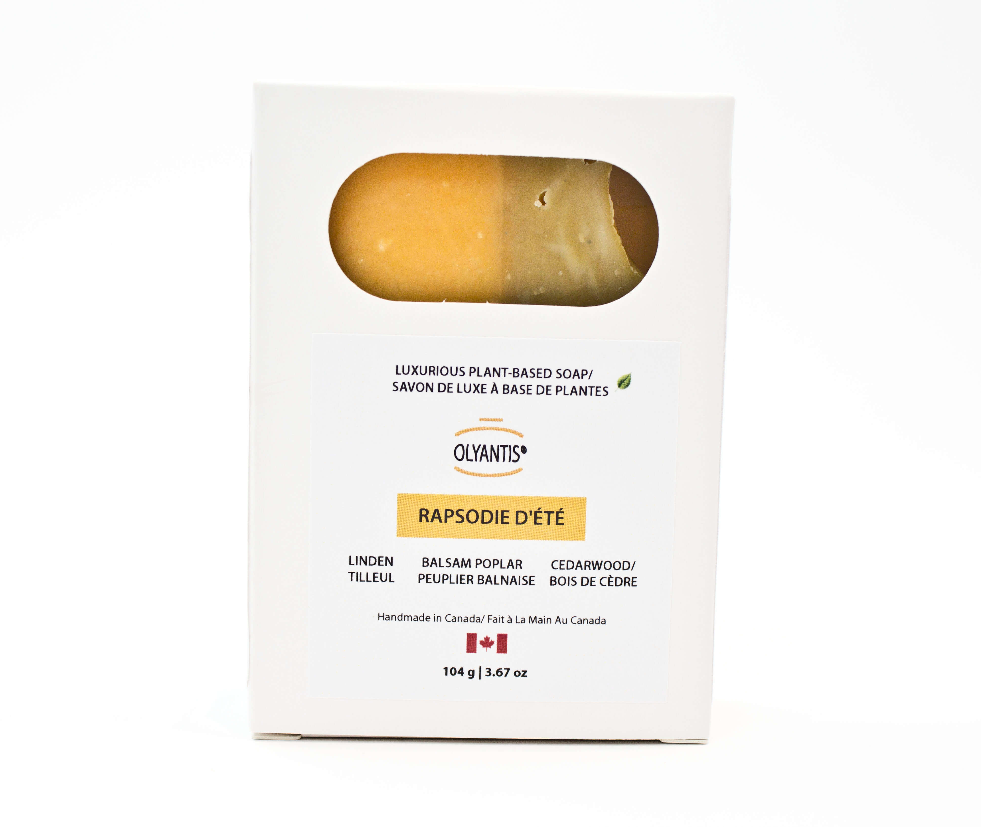 A white rectangular box of Olyantis's Rapsodie D'Eté  soap (cedarwood, linden, balsam poplar scent) with a window showing the  sage-golden-yellow bar of soap inside, set against a plain white background.